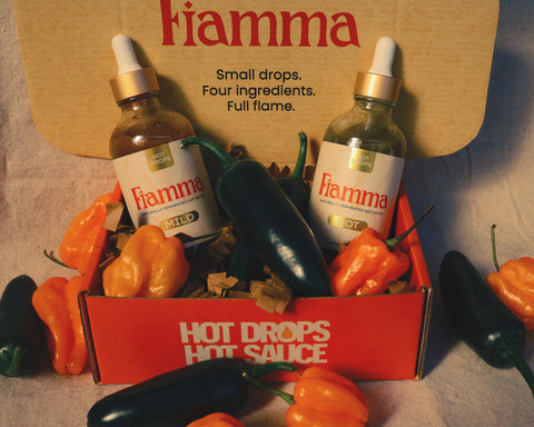 Two bottles of Fiamma hot sauce with peppers on a textured surface